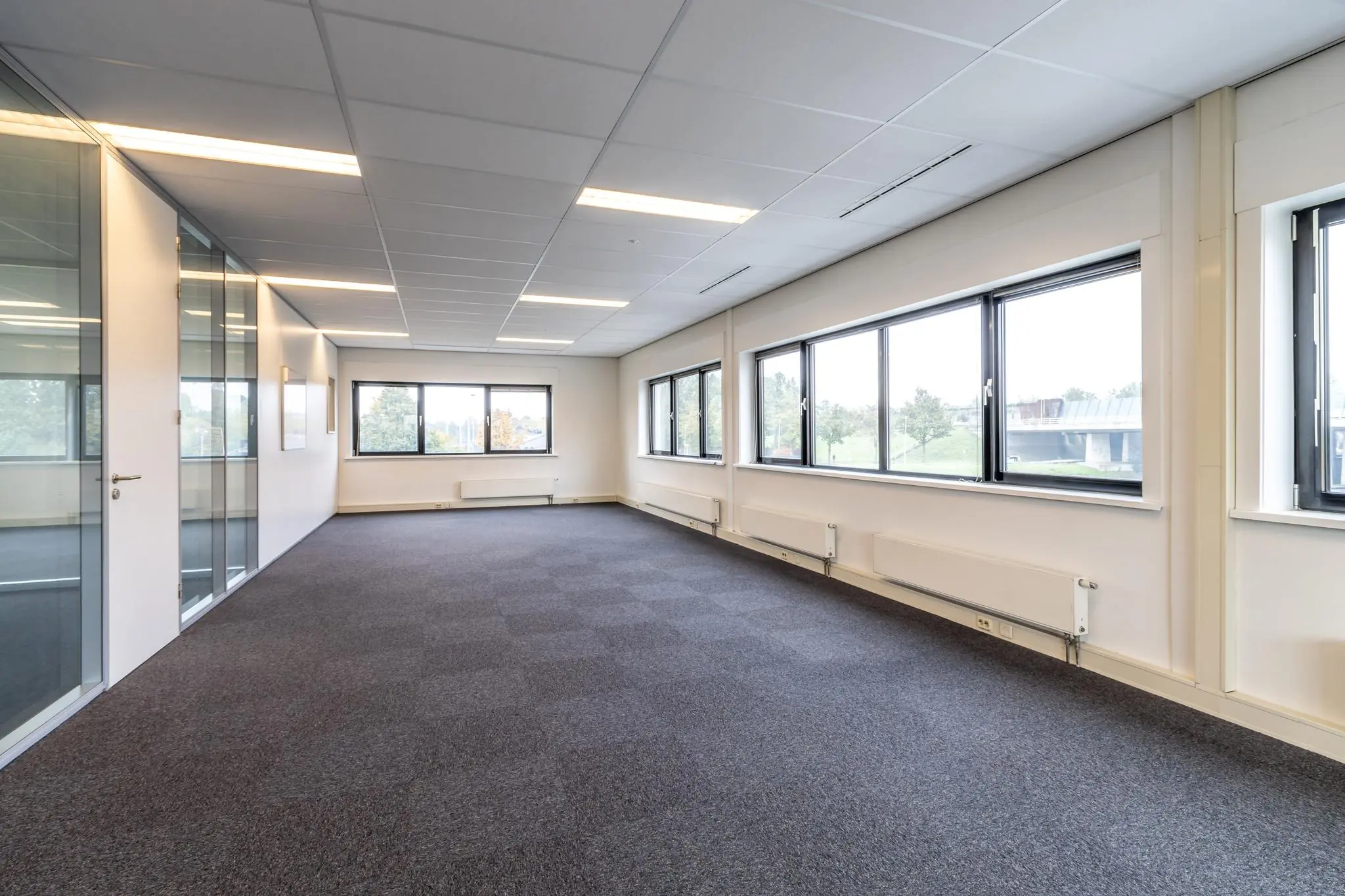 Lichte, lege kantoorruimte aan de Lage Biezenweg met grote ramen en glazen scheidingswanden.